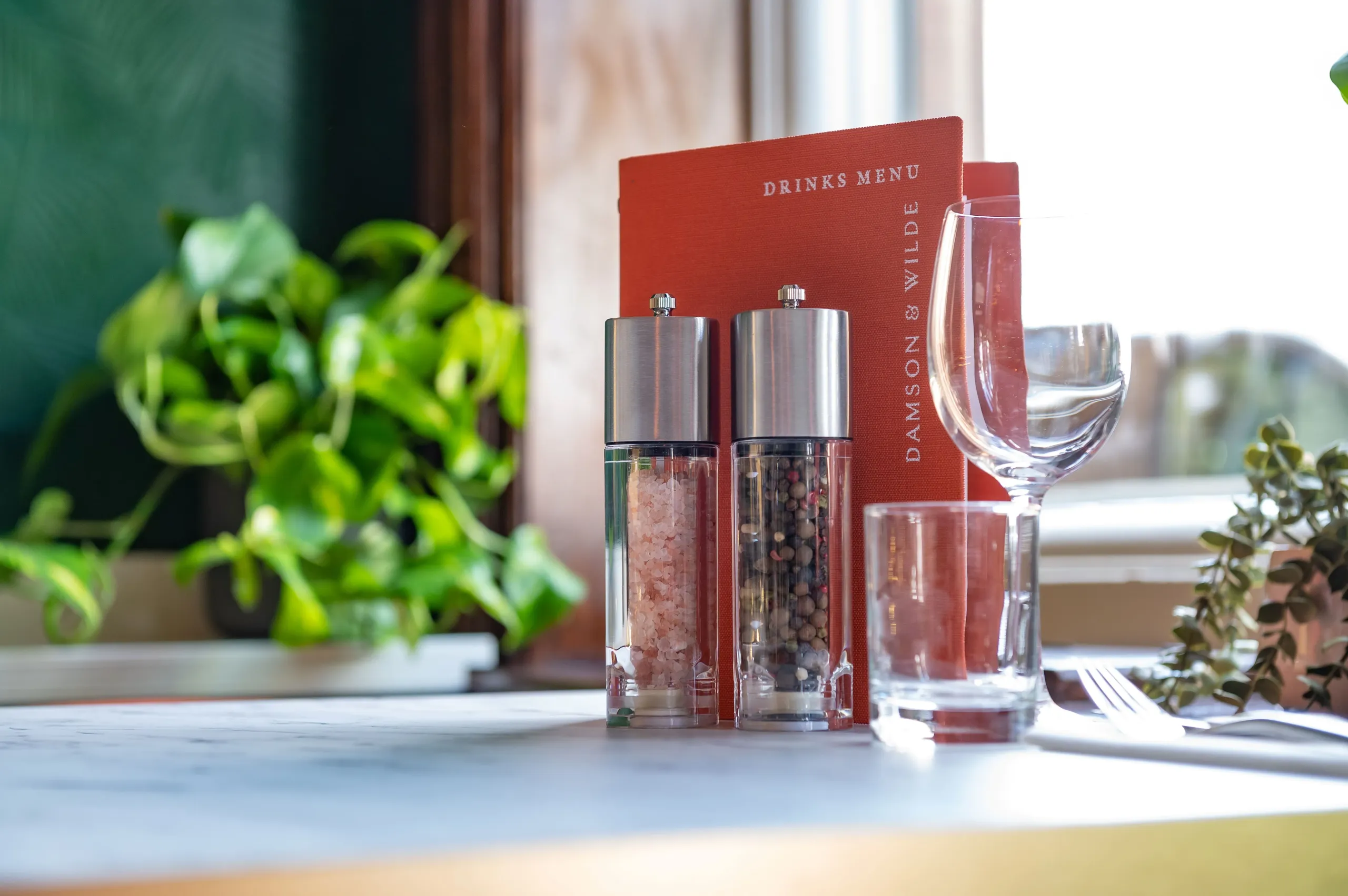 Menu, salt and pepper mills and wine glass on a window table at Damson & Wilde